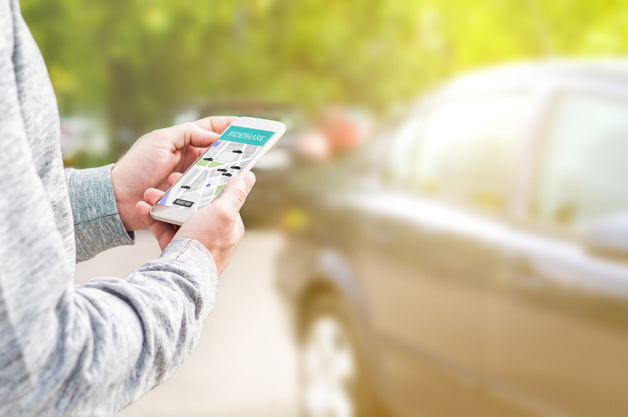 Gentleman using a mobile phone, rideshare app with a burred car in a car park in the background