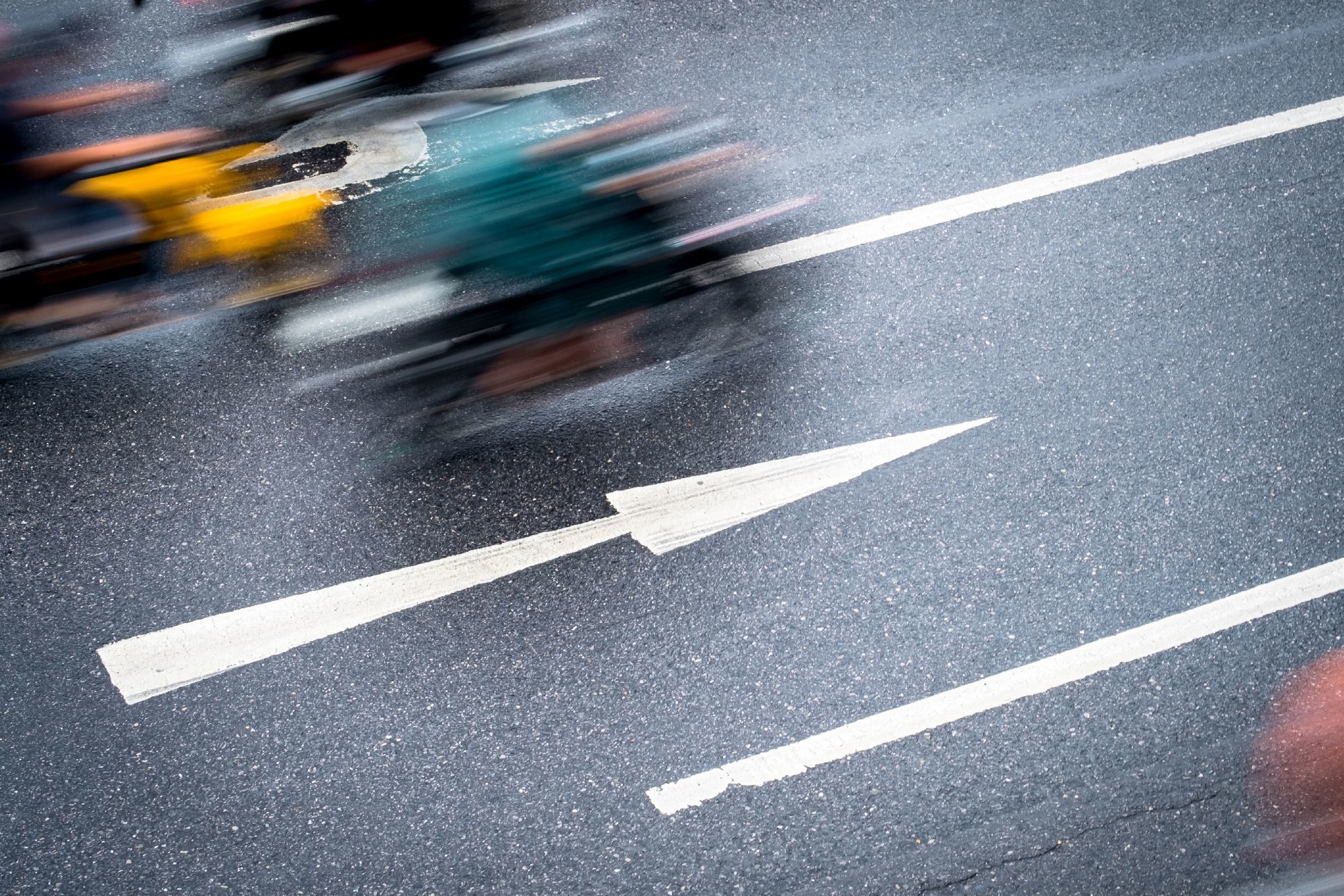 Angled view of a segement of road with right pointing arrow marking and a blurry moving motorbike