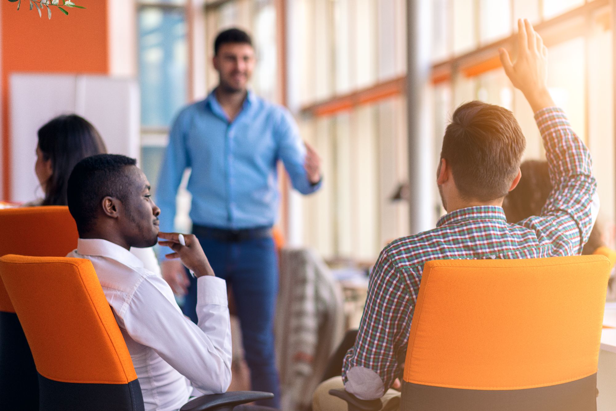 A young colleague raising hand during business meeting in an orange themed office - Professional Services