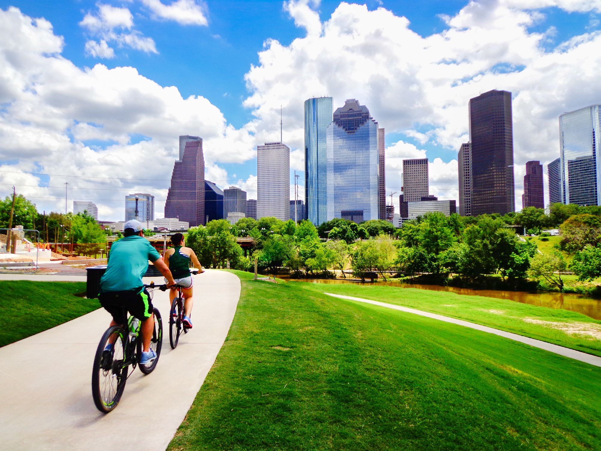 People Riding Bikes on Paved Trail in Houston Park (view of river and skyline of downtown Houston) - Change Management