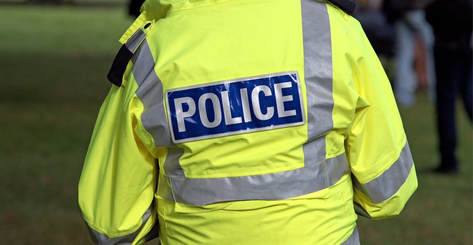 A photograph of a policeman from behind wearing a high-vis jacket with the word 'Police'